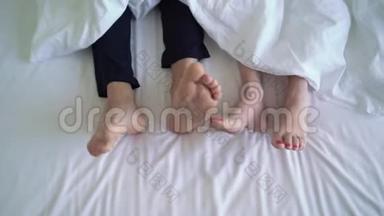 年轻夫妇在床上。 穿着羽绒被的裸腿